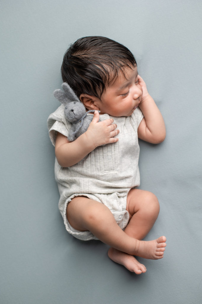 Indian newborn holding a toy bunny baby boy gentle posing blue grey and white