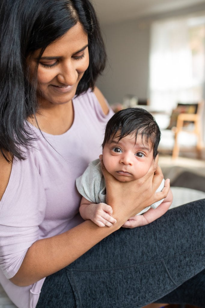 mom holding burping a newborn baby boy Indian baby looking straight at camera