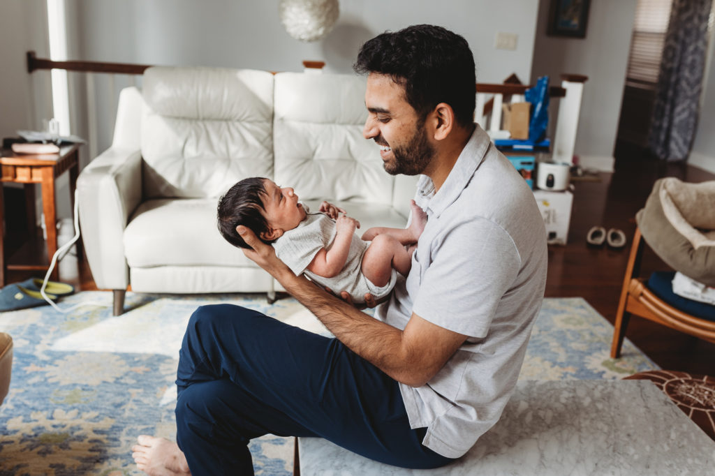 dad holding a newborn baby boy in a home session smiling profile view