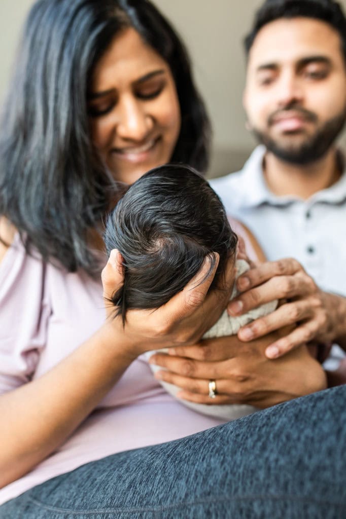 indian mom and dad holding newborn baby pose crown head newborn with hair