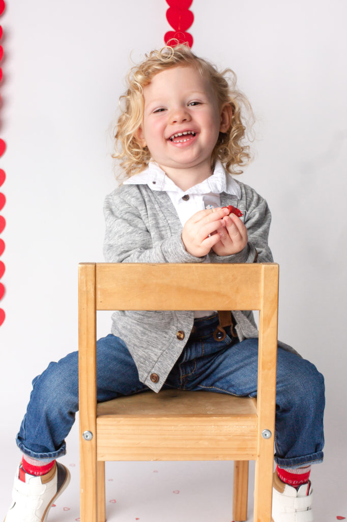 Toddler boy laughing on a chair valentines with hearts