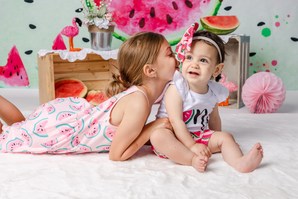 watermelon cake smash photography sisters sharing a secret with an older sister sibling