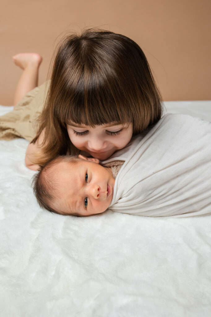 toddler sister kissing newborn brother , newborn photoshoot, brown and beige