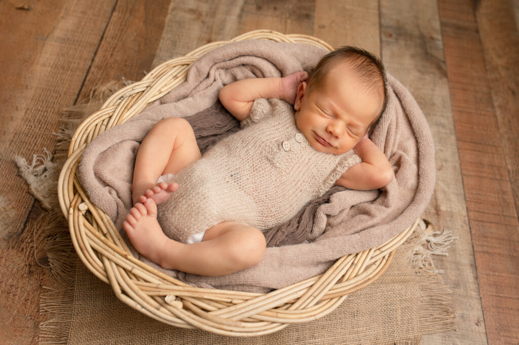 newborn boy in a basket earthy colors brown and beige smiling newborn posing